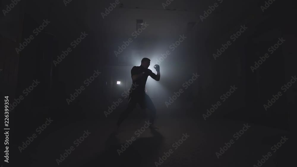 Boxer training in low light gym in slow motion. Sportsman boxing in smoky studio. Silhouette on dark background with copy space