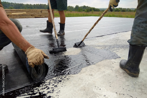Roofer worker painting bitumen praimer at concrete surface by the roller brush Waterproofing photo