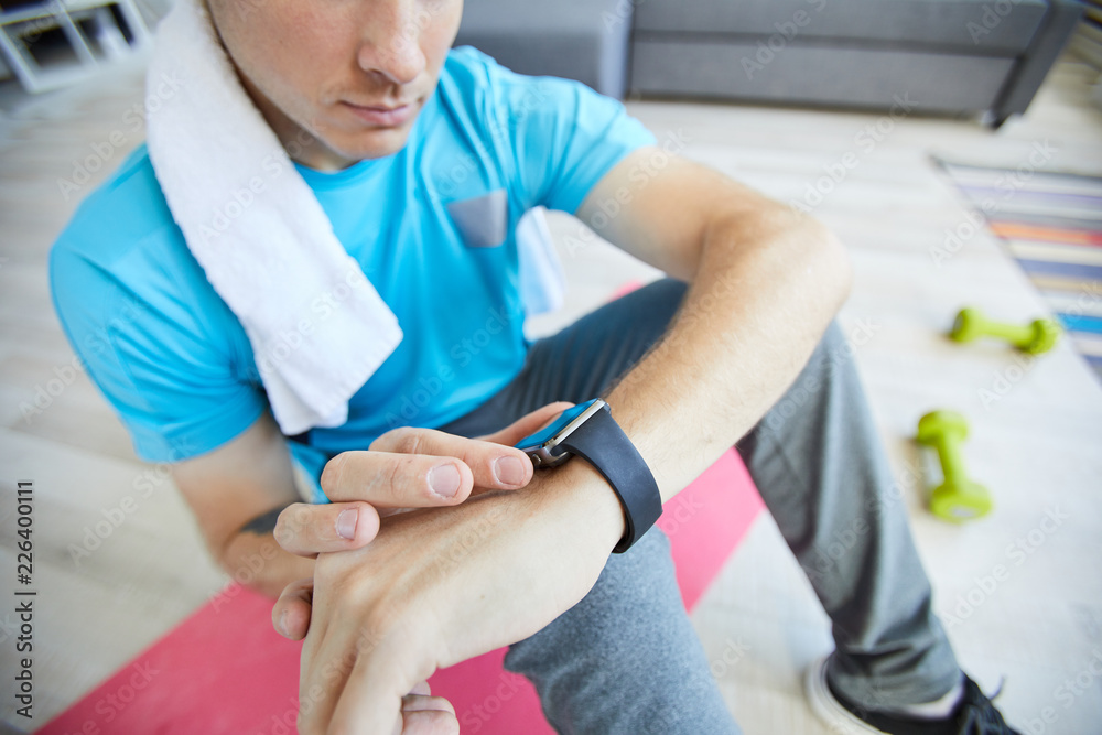 Fototapeta premium Young active man checking time in smartwatch during break between trainings