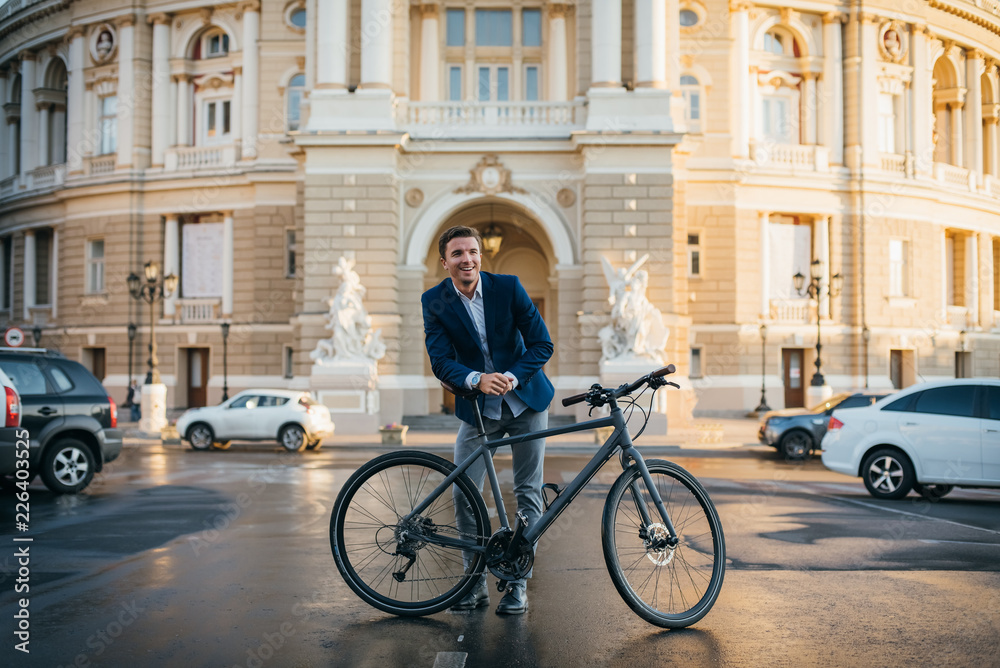 Fototapeta premium Portrait of handsome young man with his bicycle on the street in city center during sunrise
