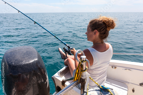 Young woman has angling excursion, sitting in boat with spinning rod