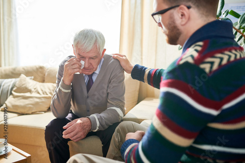Empathetic psychologist consoling senior man and stroking his shoulder while supporting him and cheering up during therapy session