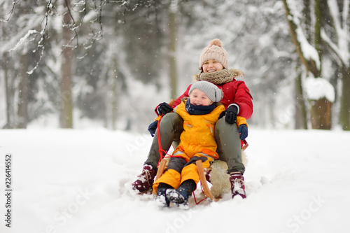 Little boy and mother sliding in the park during a snowfall photo