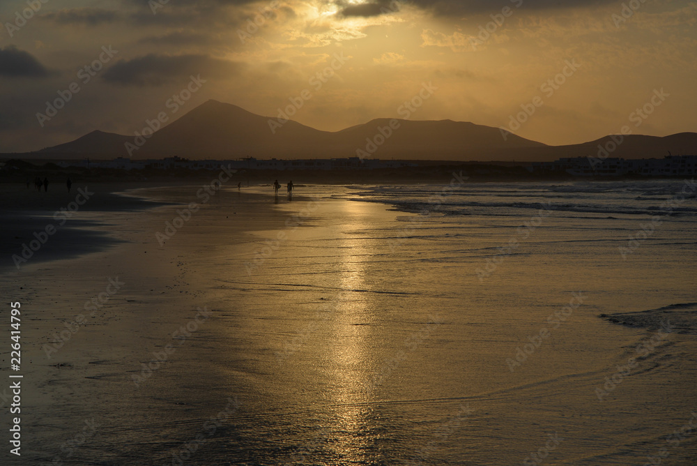 golden sunset reflected in the wet sand and silhouettes of people strolling golden sunset reflected in the wet sand and silhouettes of people strolling