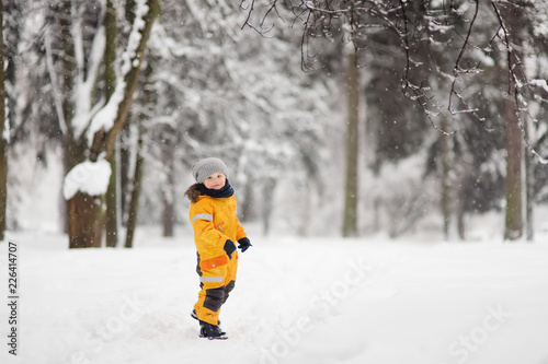 Cute little boy in yellow winter clothes walks during a snowfall © Maria Sbytova