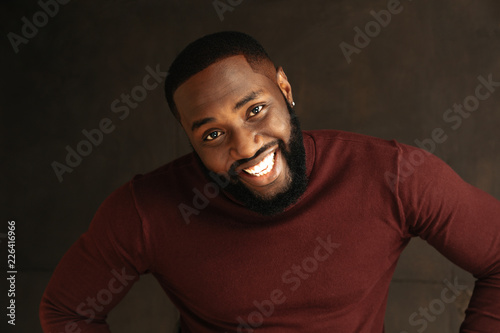 Man portrait. Style. Handsome Afro American guy in wine-colored sweatshirt is looking at camera and smiling, on a dark background