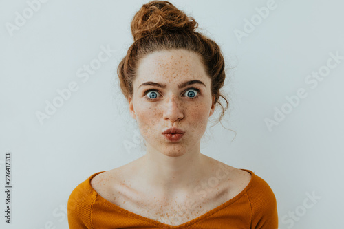 Woman portrait. Style. Beautiful blue eyed girl with freckles is pouting lips at camera, on a white background