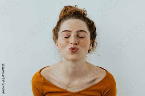 Woman portrait. Style. Beautiful girl with freckles is pouting lips at camera, on a white background