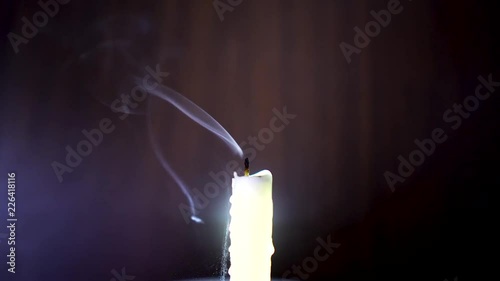 Candle isolated in a dark room illuminated slightly with a cool bluish light and being blown out watching the smoke dance rise and climb