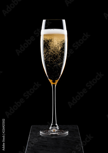 Elegant glass of yellow champagne with bubbles on black marble board on black background.