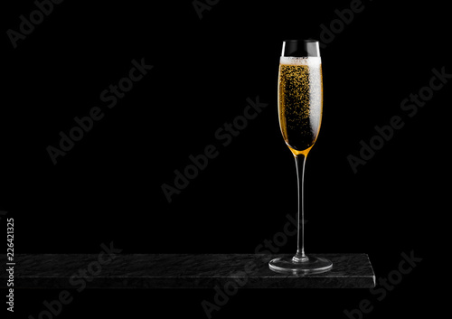 Elegant glass of yellow champagne with bubbles on black marble board on black background. Space for text
