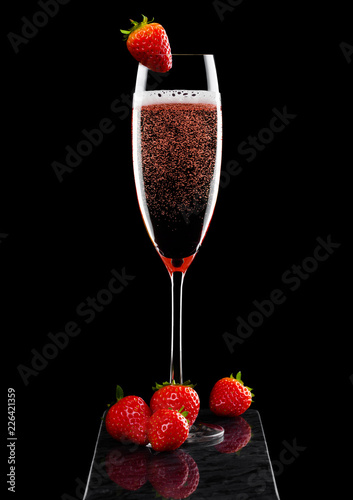 Elegant glass of pink rose champagne with strawberry on top and fresh berries on black marble board on black background.