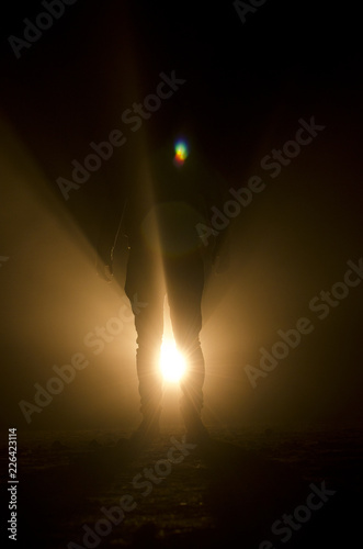 mysterious silhouette of unknown man standing in darkness illuminated from behind by spotlight photo