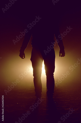 mysterious silhouette of unknown man standing in darkness illuminated from behind by spotlight