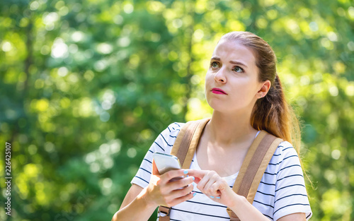 Young woman using her smartphone on a bright summer day in the forest