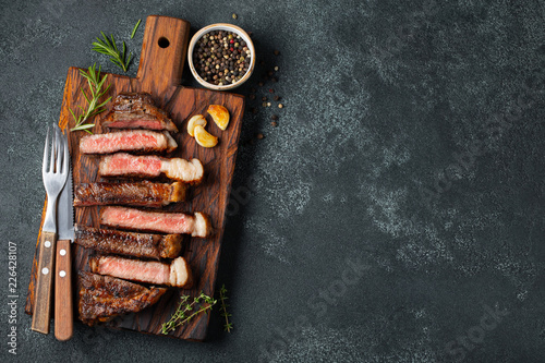 Obraz na plátně Sliced steak Striploin, grilled with pepper, garlic, salt and thyme served on a wooden chopping Board on a dark stone background
