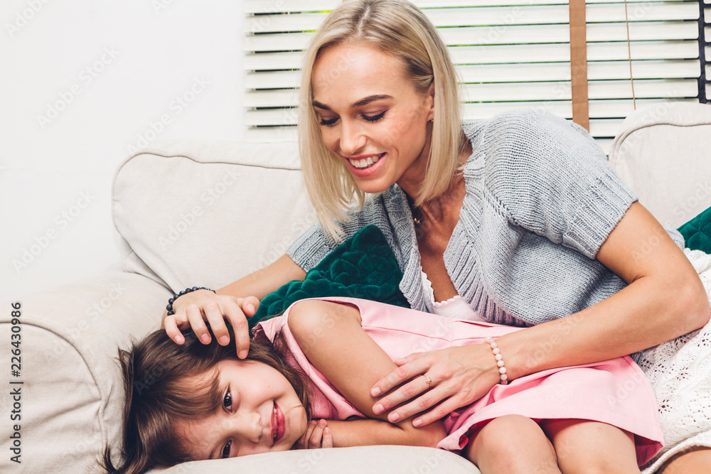 Mother with little daughter having fun and playing with mom on the sofa at home.Love of family and father day concept Mother with little daughter having fun and playing with mom on the sofa at home.Love of family and father day concept
