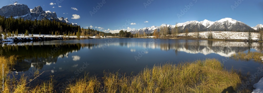 Fototapeta premium Wide Panoramic Landscape of Blue Quarry Lake and Snowy Rocky Mountain Peaks above City of Canmore near Banff National Park Alberta Canada