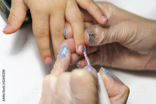 Professional manicure for child. Cosmetologist applies healing and firming varnish on nails on child s fingers. Shooting close-up.