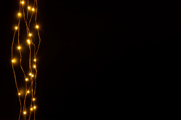 Christmas lights garland border over black background. Flat lay, copy space.