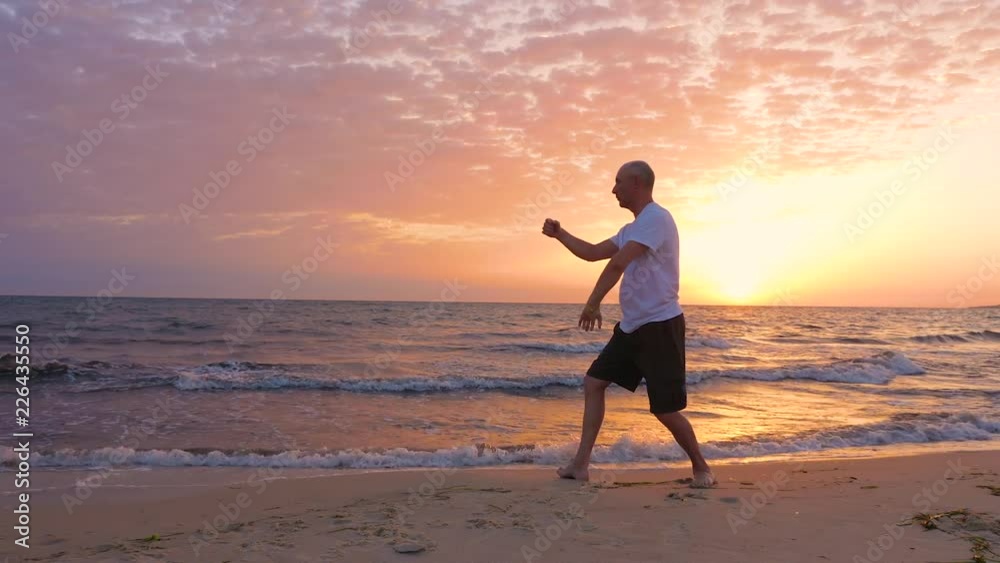 Athletic man practicing Tai Chi asian martial arts on sea beach in the morning Athletic man practicing Tai Chi asian martial arts on sea beach in the morning