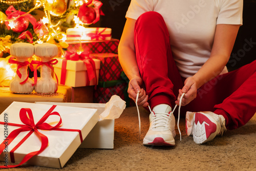 Fototapeta Naklejka Na Ścianę i Meble -  Woman in pajamas ties the laces of athletic shoes. Christmas Present. Birthday Present.