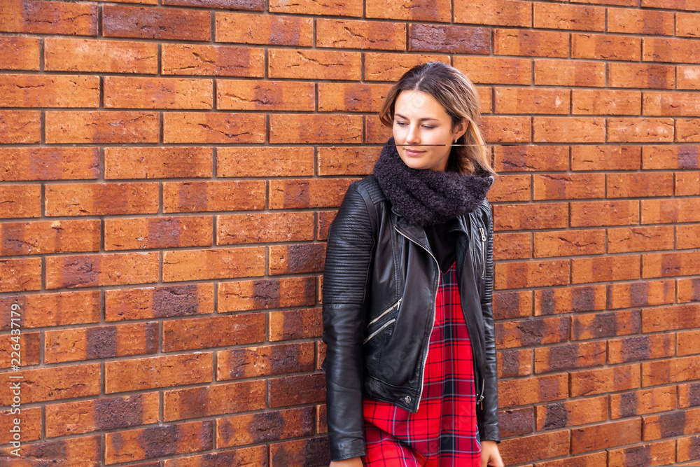 portrait of young trendy woman dressed in black coat and red knitted hat stay around brick wall, look away, enjoy vacation in the old city, autumn street fashion. portrait of joyful woman portrait of young trendy woman dressed in black coat and red knitted hat stay around brick wall, look away, enjoy vacation in the old city, autumn street fashion. portrait of joyful woman