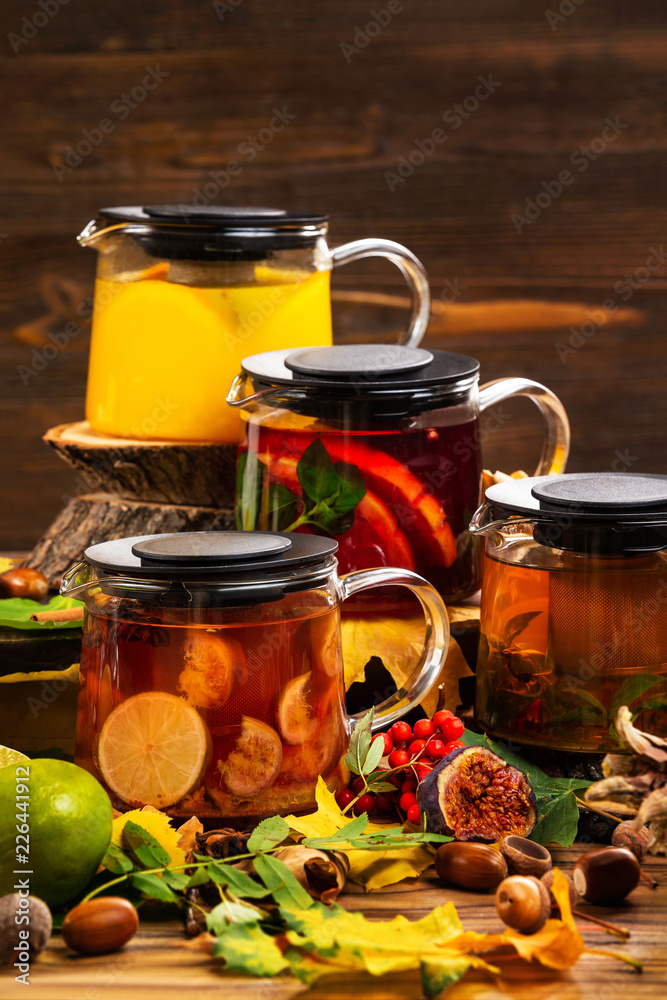 Vertical iimage of teapots set with different colorful natural tea decorated with autumn leaves at wooden dark board background. Vertical iimage of teapots set with different colorful natural tea decorated with autumn leaves at wooden dark board background.