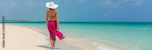 Luxury travel vacation elegant lady walking on beach in pink fashion skirt wrap relaxing on Caribbean holidays during winter. Panoramic banner landscape crop for background.