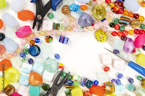 An overhead photo of many different beads with tools for making jewellery, on a white background with a place for text