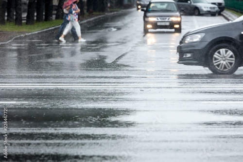 city car traffic during the rain. pedestrians crossing wet road. cars in motion