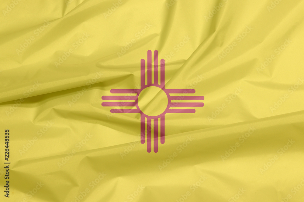 Fabric flag of New Mexico. Crease of New Mexico flag background, The states of America, The red and yellow of old Spain. The ancient Zia Sun symbol in red. Fabric flag of New Mexico. Crease of New Mexico flag background, The states of America, The red and yellow of old Spain. The ancient Zia Sun symbol in red.