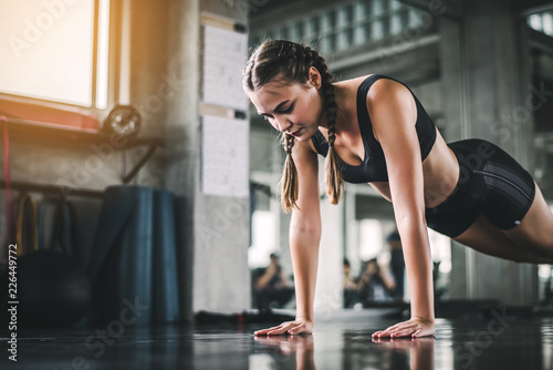 Fototapeta Naklejka Na Ścianę i Meble -  Cinematic tone of young attractive fitness woman exercise with machine in gym. Individual sport to fit muscles of body for healthy life concept. 