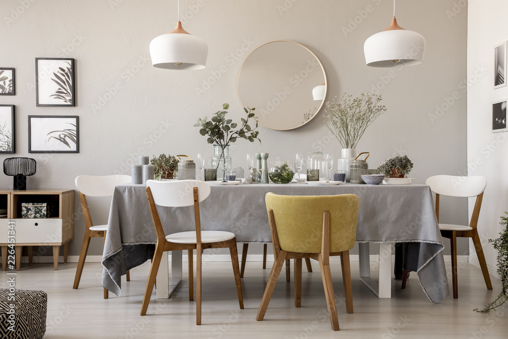 Wooden chairs at table with tableware in dining room interior with lamps and round mirror. Real photo - obrazy, fototapety, plakaty 