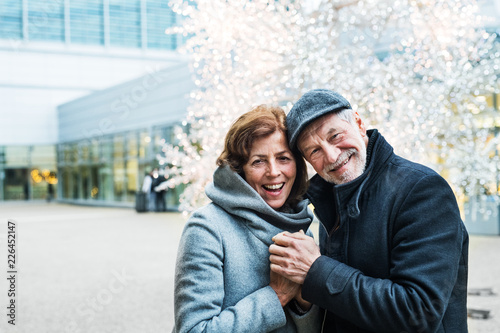 A senior couple standing outdoors in front of shopping center at Christmas time.
