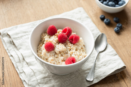 Oatmeal porridge with berry fruits on linen textile. Healthy breakfast food, dieting and healthy eating concept