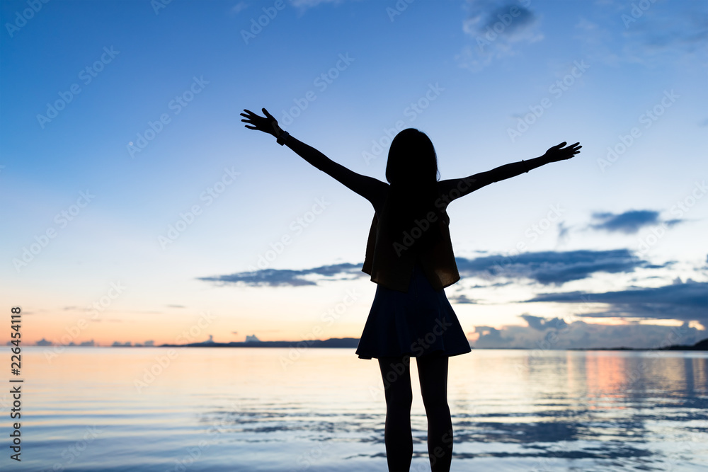 Silhouette of woman raising hand at sunset time
