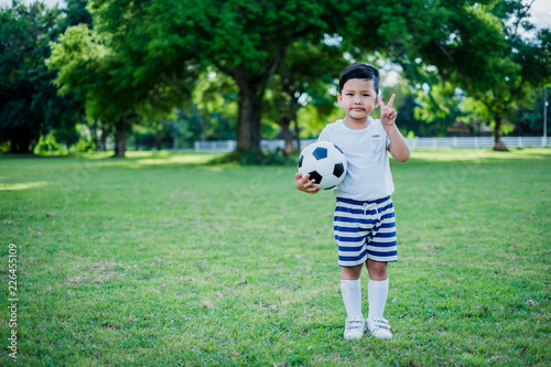 Little Asian child hand holding football and playing soccer on grass