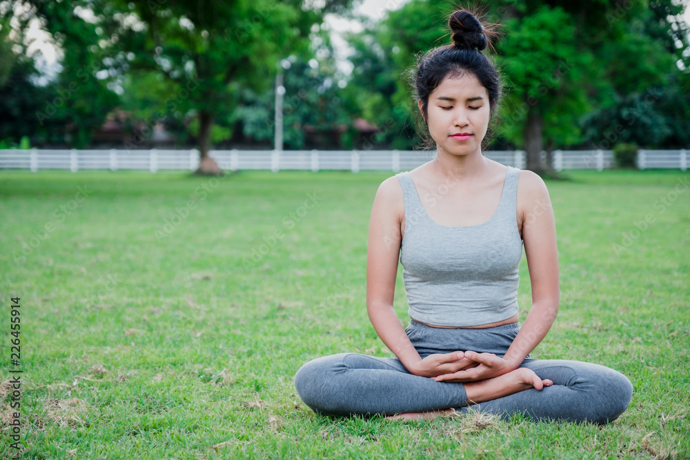 Asian woman practices yoga on meadow in the park.Yoga concept