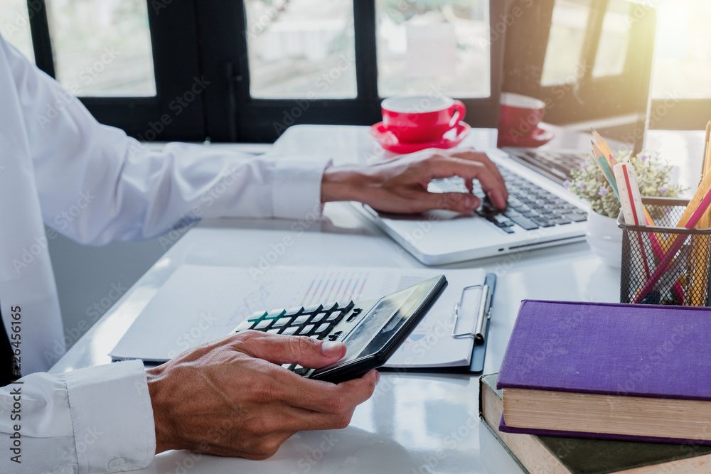 Fototapeta premium Businessman hand working with financial data and calculator on white desk in modern office.Business analysis and strategy concept.