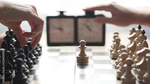 Two players play chess. Closeup of chessboard and clock. Players take turns moving chess pieces and pushing the clock button to stop time.