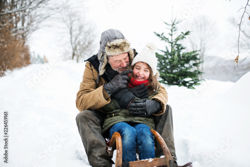 фотографія Grandfather and small girl sledging on a winter day.