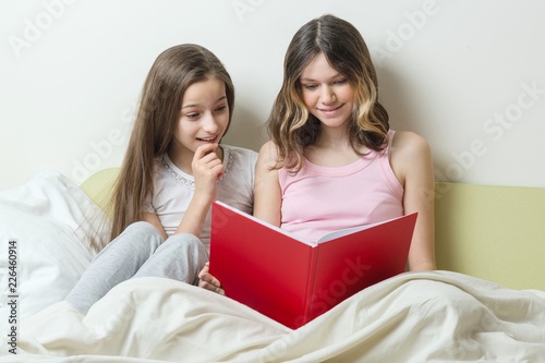 Two teenage girls sitting at home in bed look in school notebook. Communication and learning at home