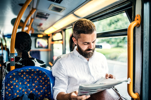 Hipster man on a bus in the city, travelling to work and reading newspapers. photo