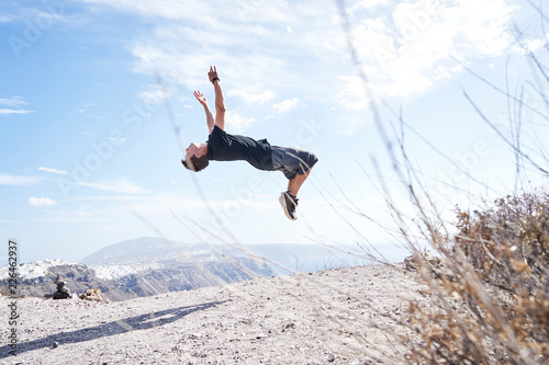 Mann macht Parkour und springt einen Salto vor der Küste Santorins 