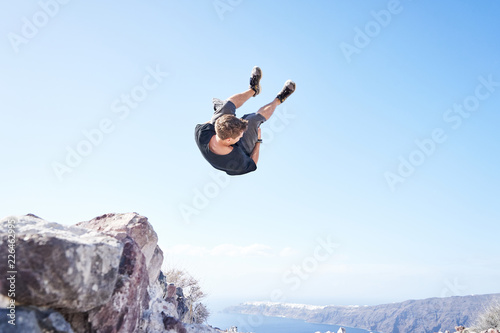 Mann macht Parkour und springt einen Salto vor der Küste Santorins 