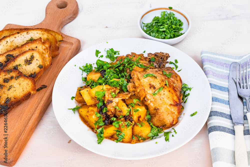 Fototapeta premium Italian food - stewed chicken with potatoes in tomato sauce on a plate and toasted bread, close-up