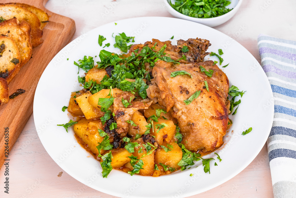 Italian food - stewed chicken with potatoes in tomato sauce on a plate and toasted bread, close-up Italian food - stewed chicken with potatoes in tomato sauce on a plate and toasted bread, close-up