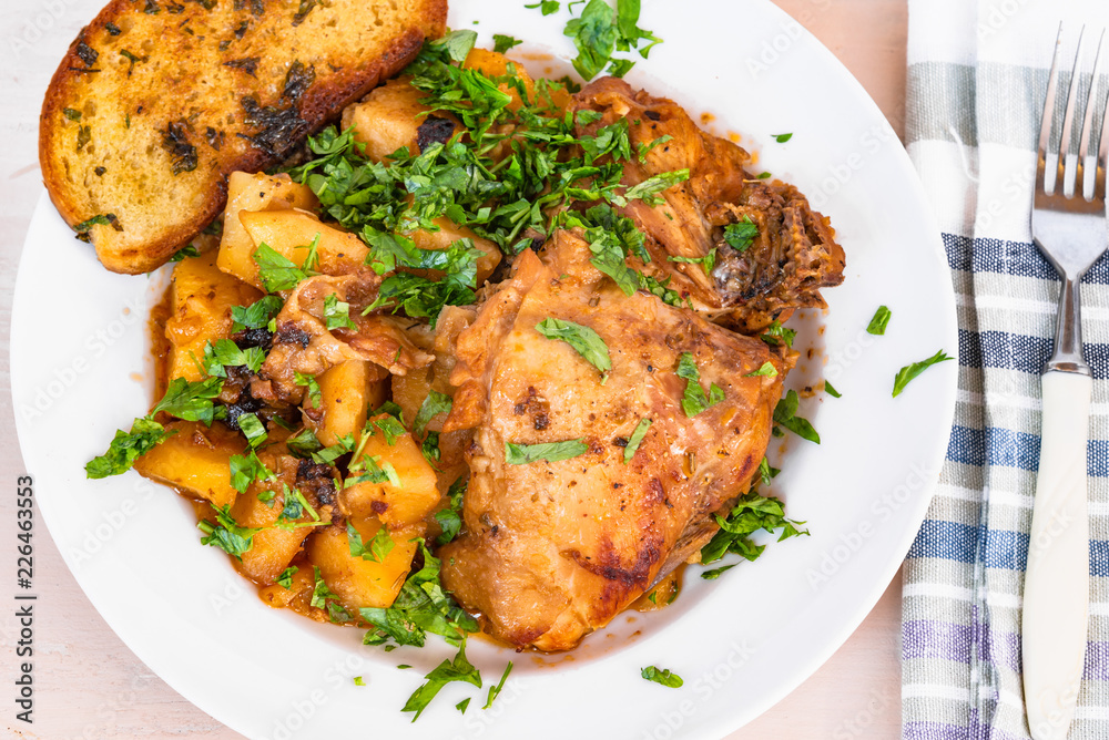 Italian food - stewed chicken with potatoes in tomato sauce on a plate and toasted bread, close-up