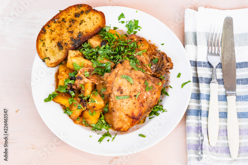 Italian food - stewed chicken with potatoes in tomato sauce on a plate and toasted bread, close-up